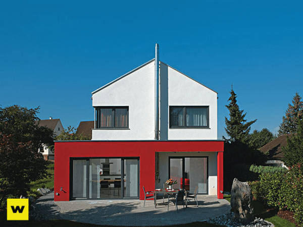 Modernes Einfamilienhaus mit roter Fassade, großer Fensterfront und Garten im Sonnenlicht.