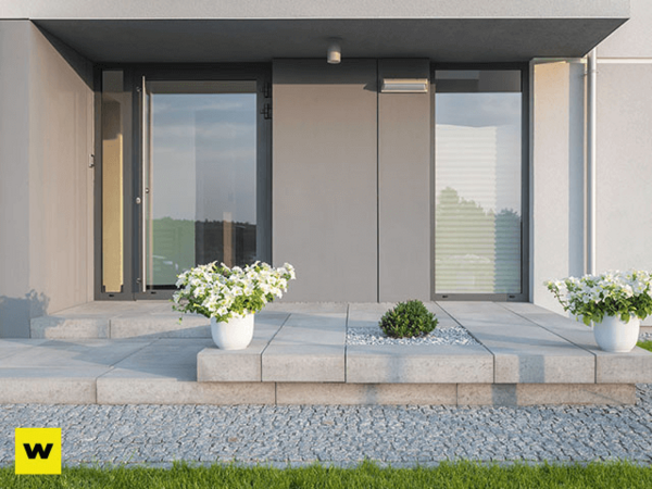 Moderner Hauseingang mit grauen Fliesen, großen Fenstern und weißen Blumenkübeln.