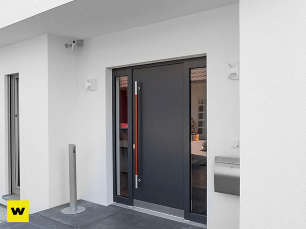 Moderne Haustür aus Aluminium mit seitlichem Glas und Edelstahlgriff an weißer Fassade.