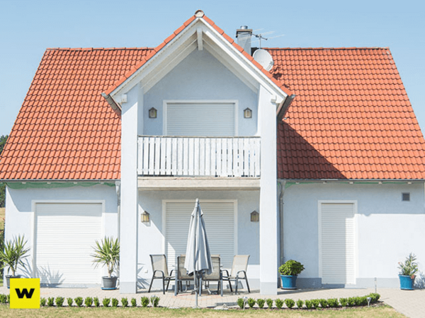 Modernes Einfamilienhaus mit rotem Dach, Balkon und Terrasse im Sonnenschein.